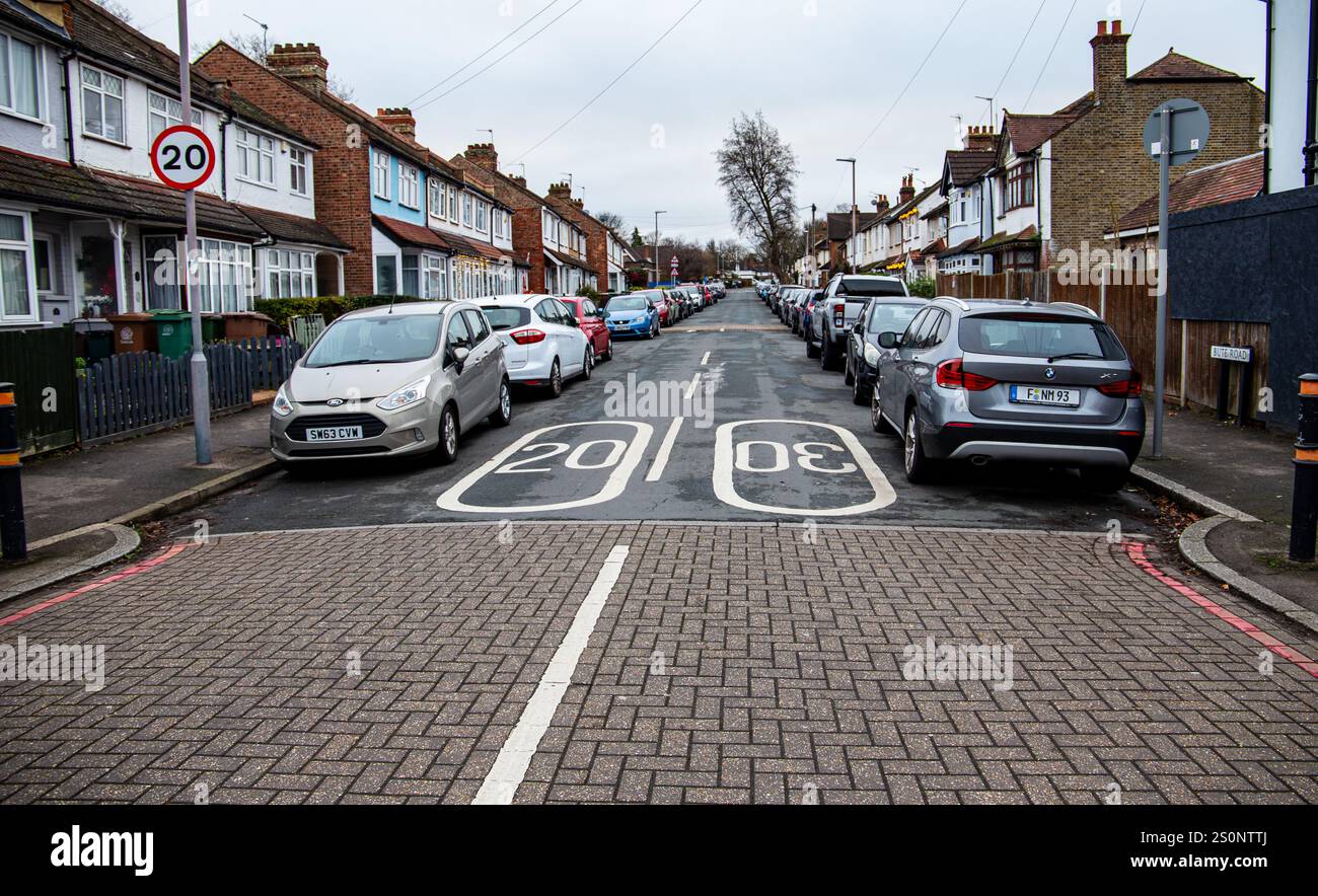 Strada residenziale urbana fiancheggiata da auto parcheggiate, con segnaletica per il limite di velocità di 20 km/h e tipiche case a schiera britanniche Foto Stock