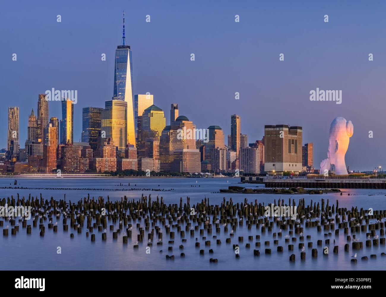 Lo skyline della città è inondato di luce dorata mentre il sole tramonta, con una grande e distintiva scultura, Water's Soul, visibile sulla destra. Pali in legno pro Foto Stock