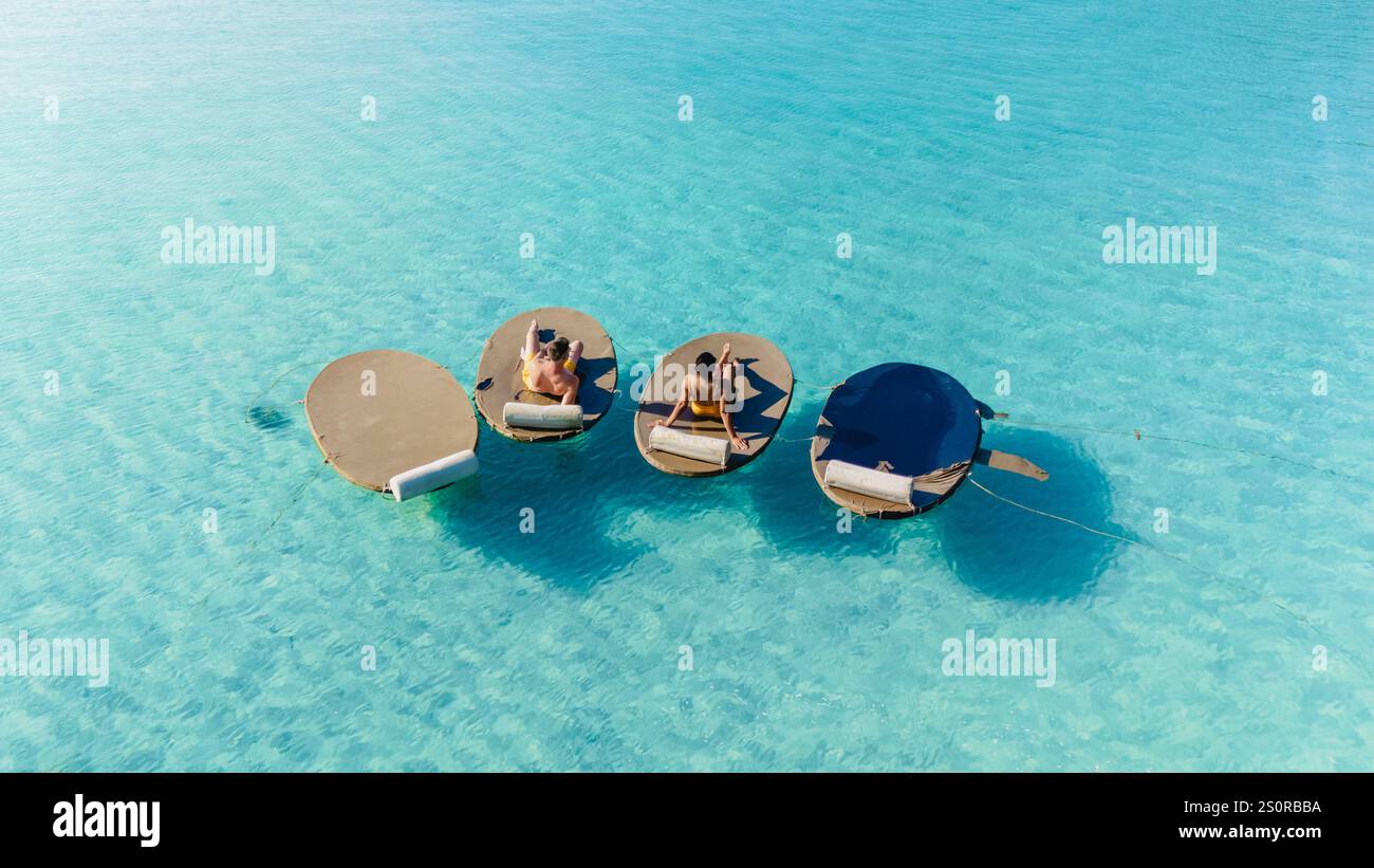 Due persone si rilassano su lettini galleggianti nelle invitanti acque turchesi di Koh Kood, Thailandia. La luce del sole splende sulla superficie, creando un'atmosfera tranquilla per il relax. Foto Stock