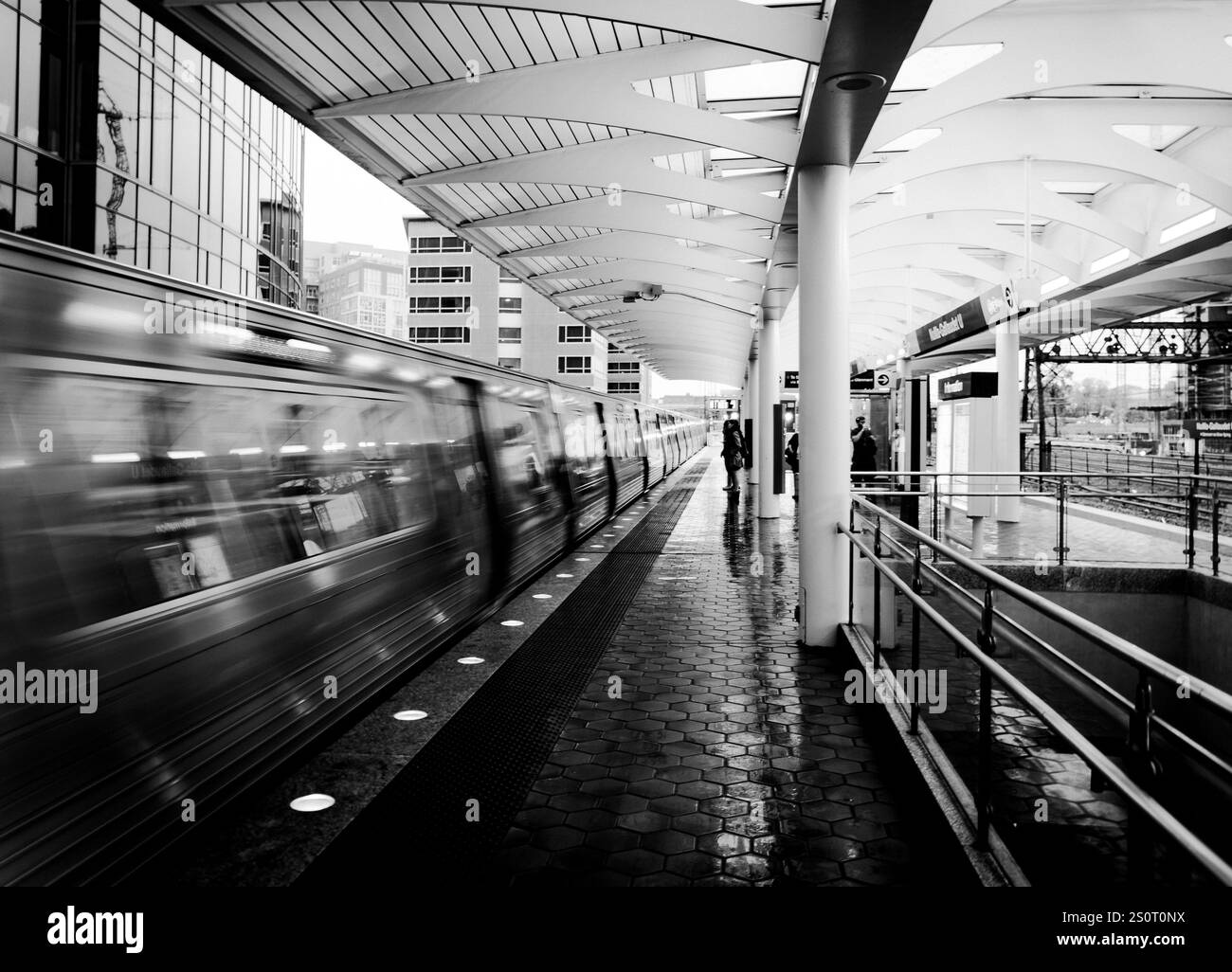 Una fotografia in bianco e nero di una piattaforma della stazione della metropolitana con un treno in movimento. La scena cattura il movimento dinamico del treno e del trampolino Foto Stock