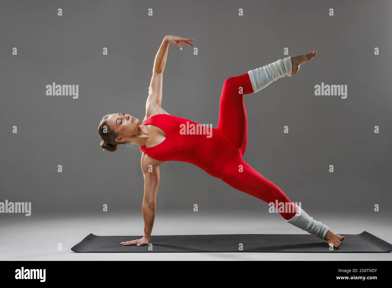 Donna in abbigliamento sportivo rosso che fa vasisthasana, posa su un tappeto interno. Pratica yoga e concetto di stile di vita sano. Foto Stock