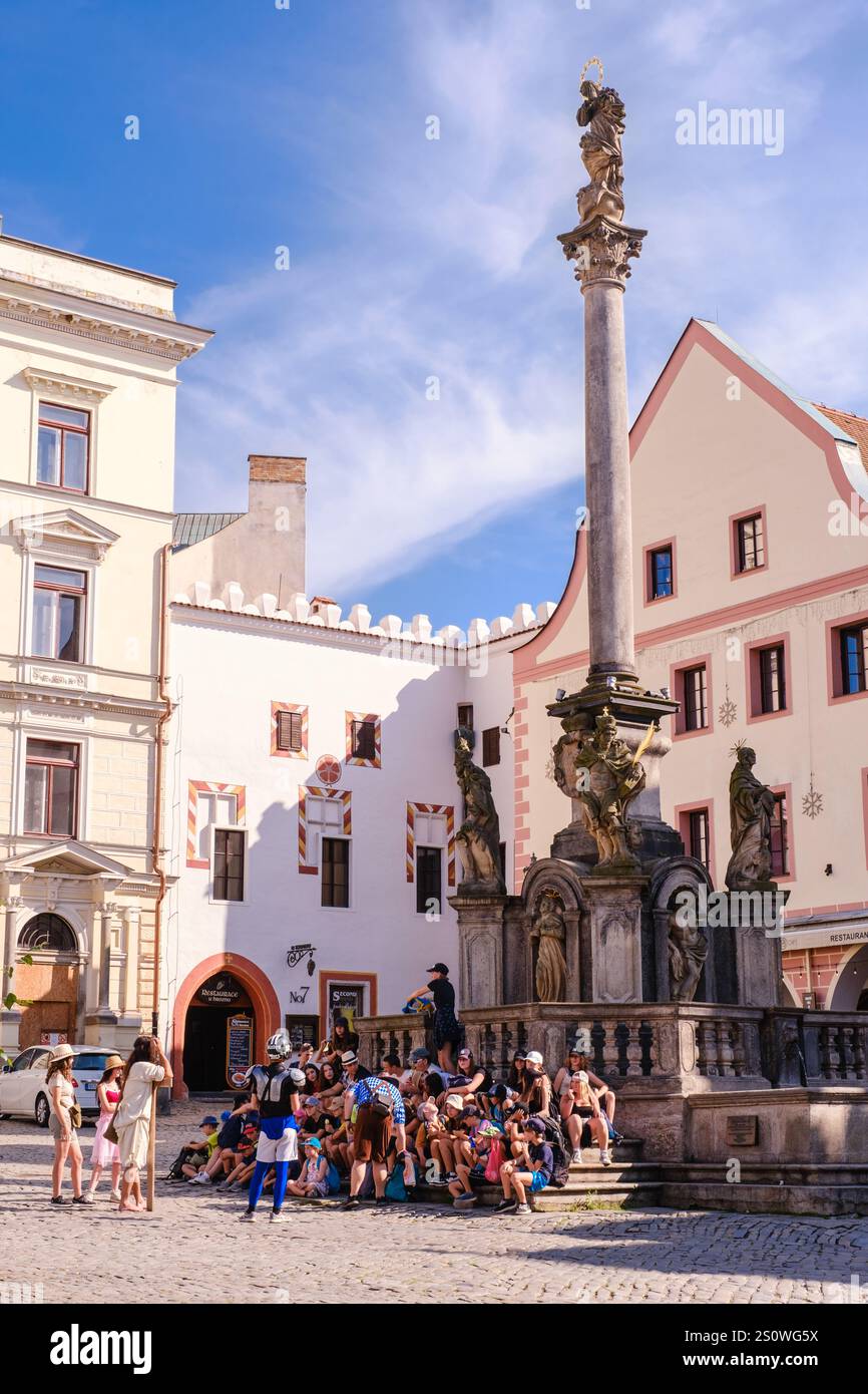 Cesky Krumlov, turisti nella piazza principale che riposano alla base della colonna della peste e della Fontana circostante, Repubblica Ceca, Cechia. Foto Stock