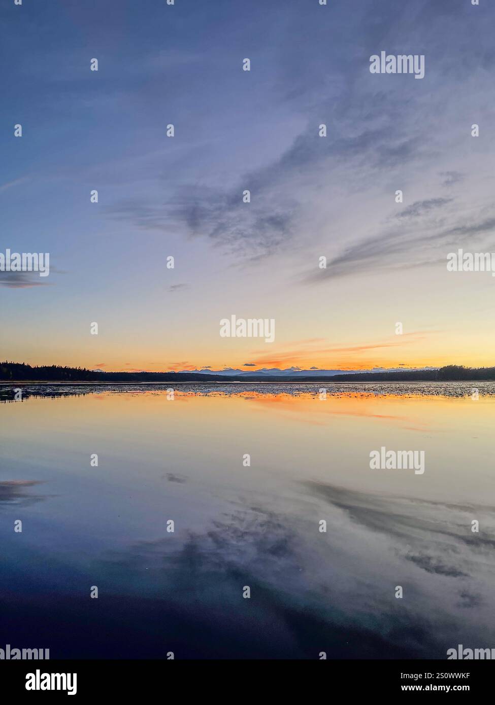 Un lago panoramico riflette i caldi colori del tramonto, con morbide nuvole e un cielo tranquillo e ampio. - Immagine stock catturata con smartphone