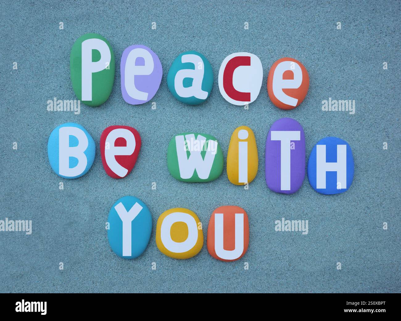 Pace sia con te, slogan sociale composto da lettere in pietra dipinte a mano multicolore su sabbia verde Foto Stock