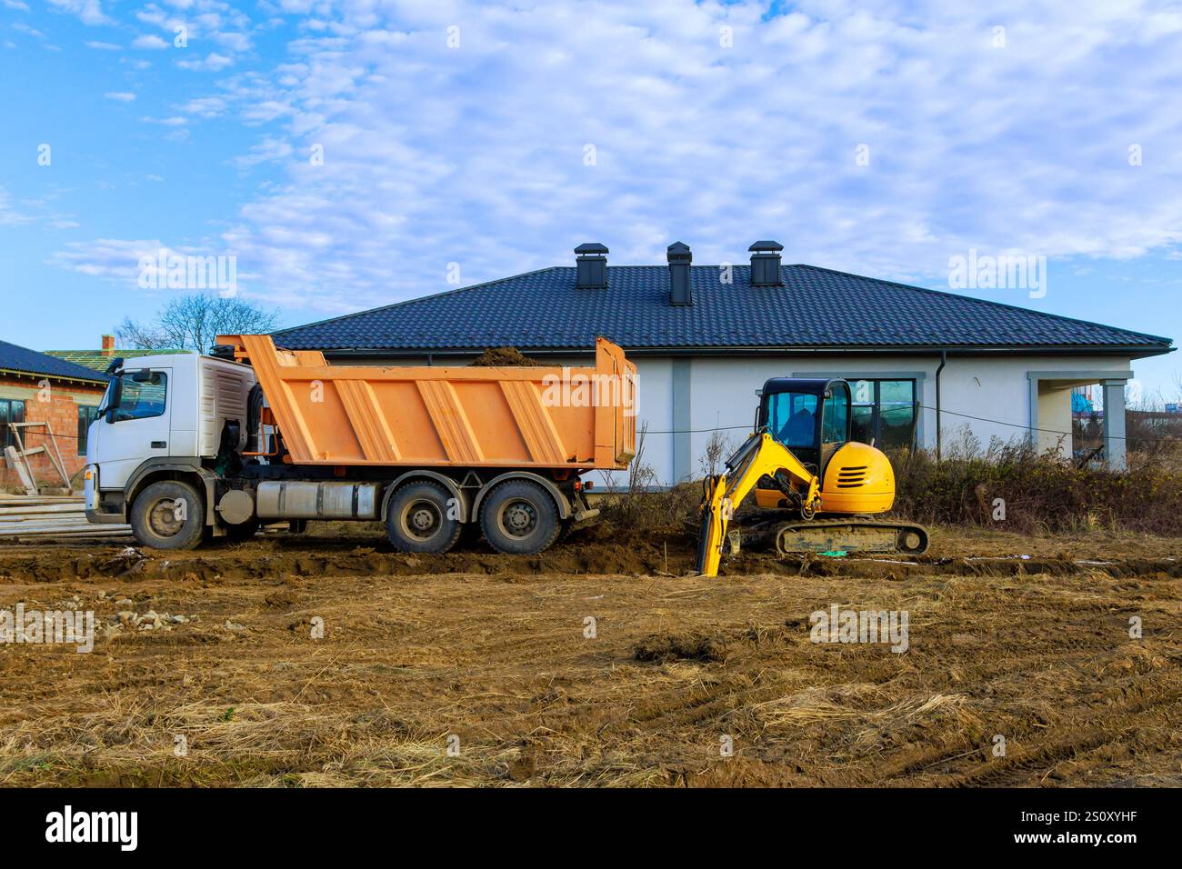 I lavoratori utilizzano dumper e escavatori per preparare il terreno per una nuova casa nell'area suburbana. Foto Stock