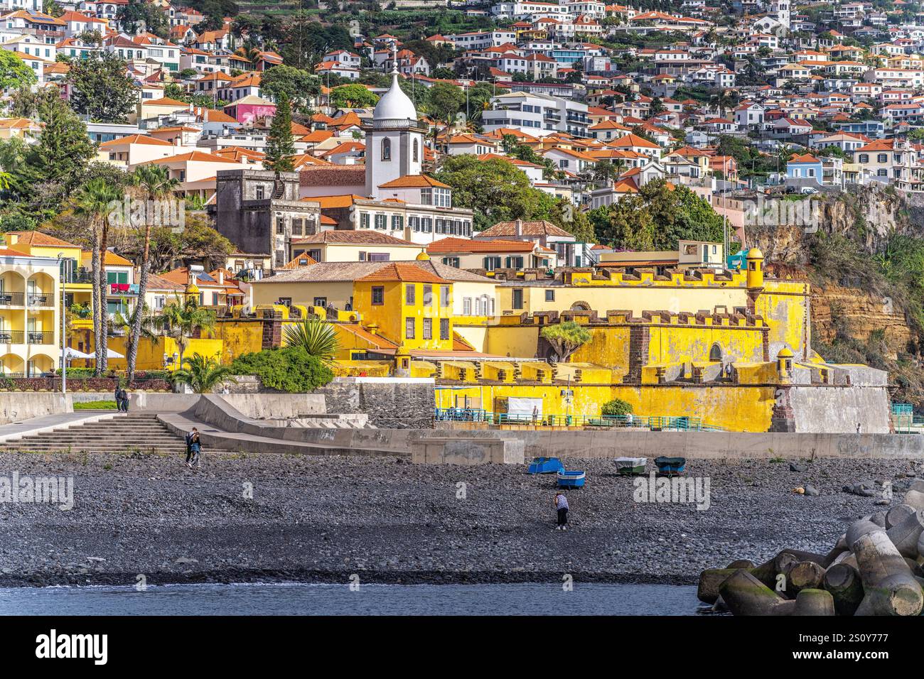 Colorata scena costiera che mostra un forte giallo sul mare circondato da vivaci case del villaggio. Foto Stock