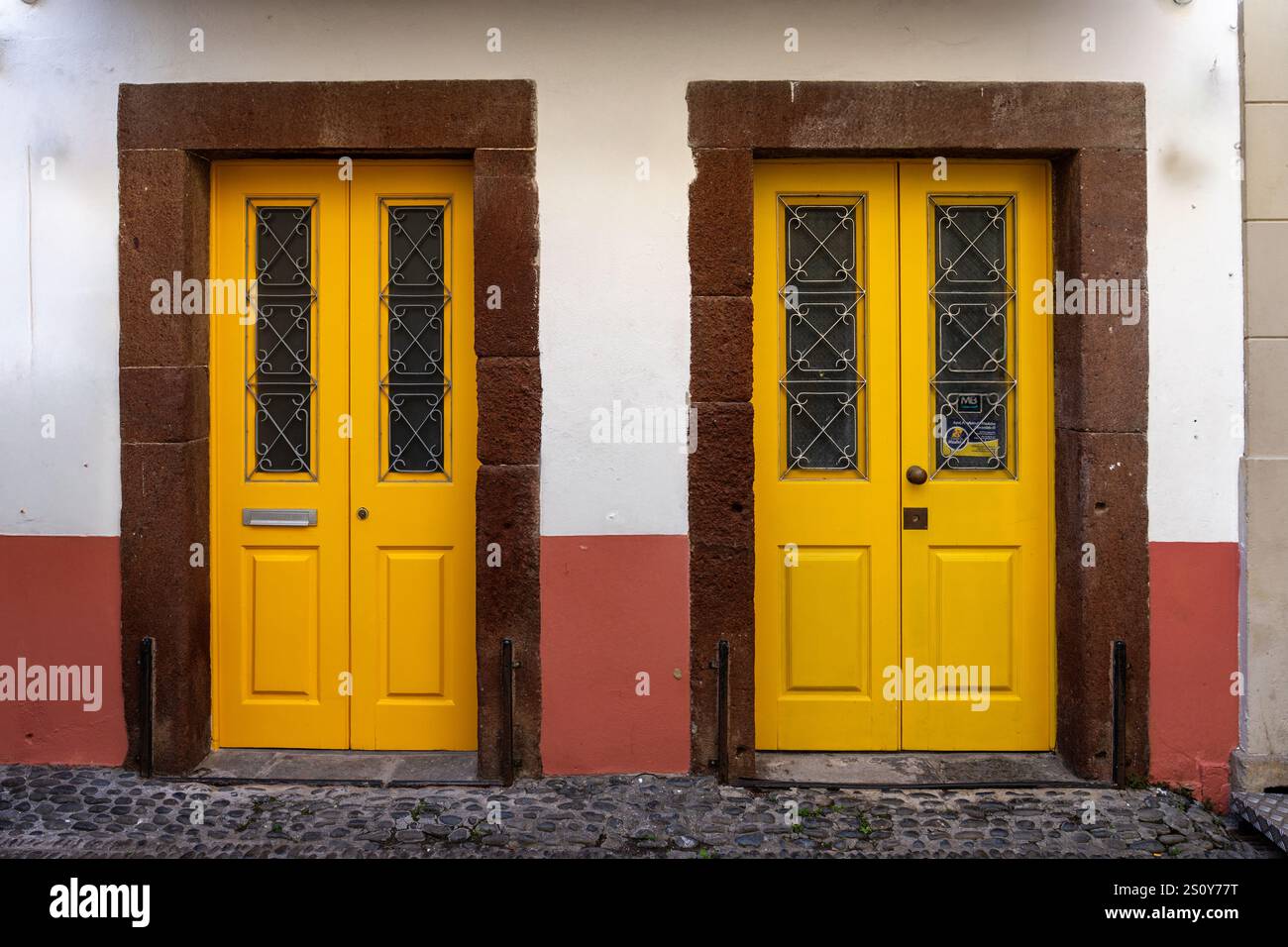 Porte gialle gemelle colorate con disegni intricati incorniciati da pietra rossa, che trasmettono fascino mediterraneo. Foto Stock