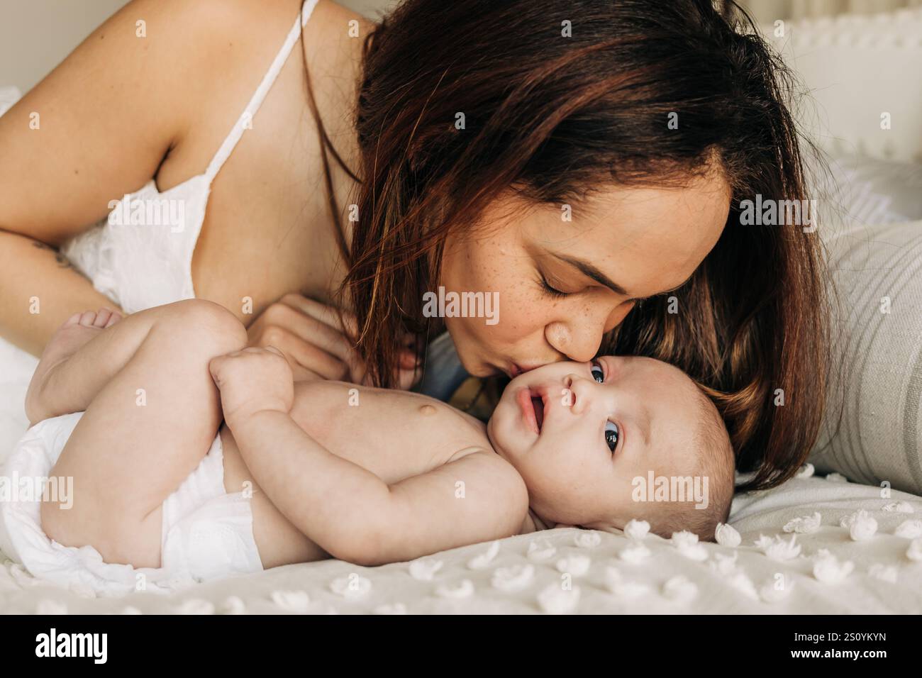 Madre che baciava amorevolmente il suo bambino mentre sdraiata su un letto accogliente Foto Stock