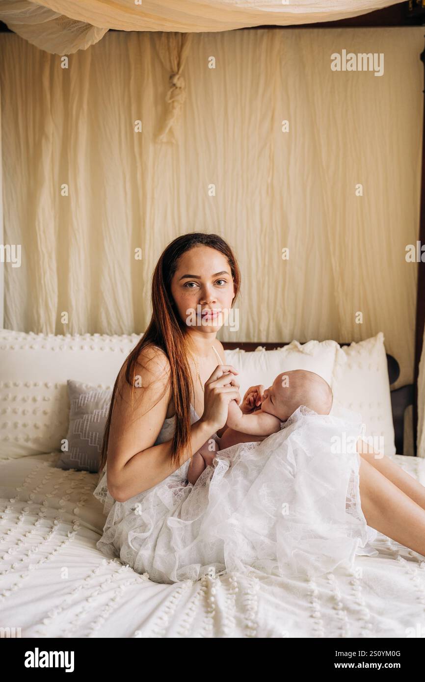 Madre che tiene il bambino in una camera da letto serena, caratterizzata da toni morbidi e neutri Foto Stock