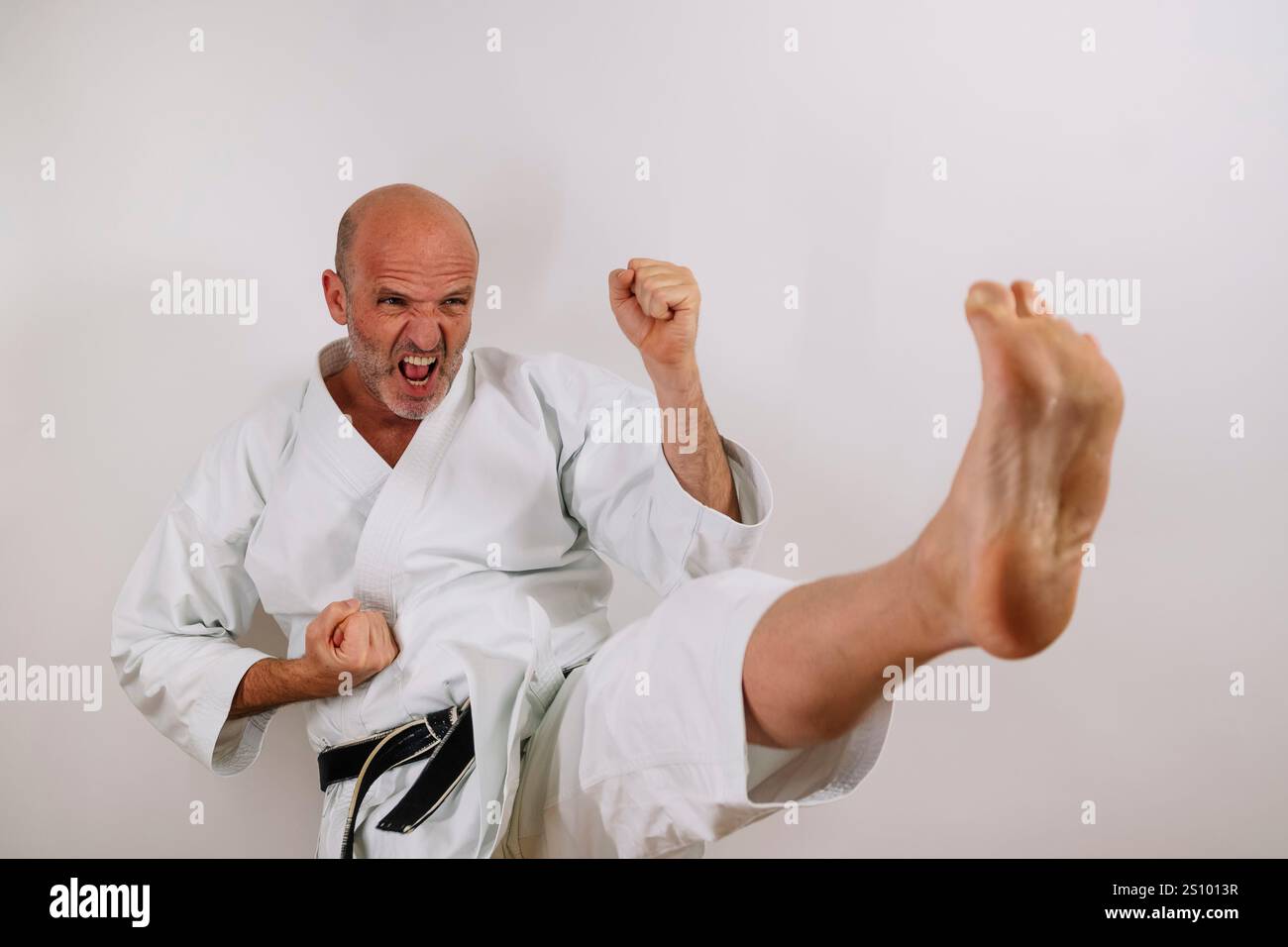 Karateka senior che esegue un calcio potente, una concentrazione intensa. Foto Stock