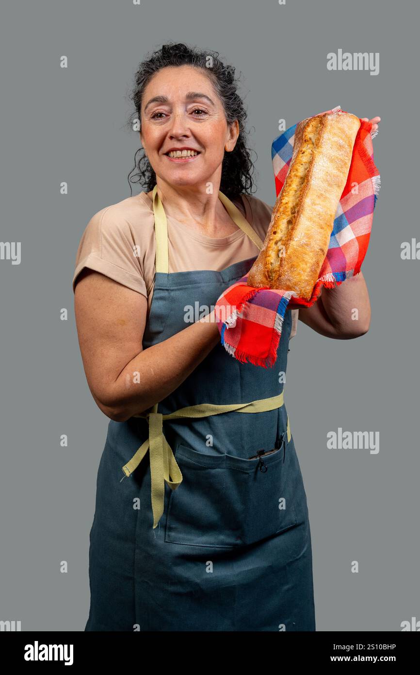 Donna fornaio sorridente che tiene il pane appena sfornato avvolto in un panno a scacchi Foto Stock