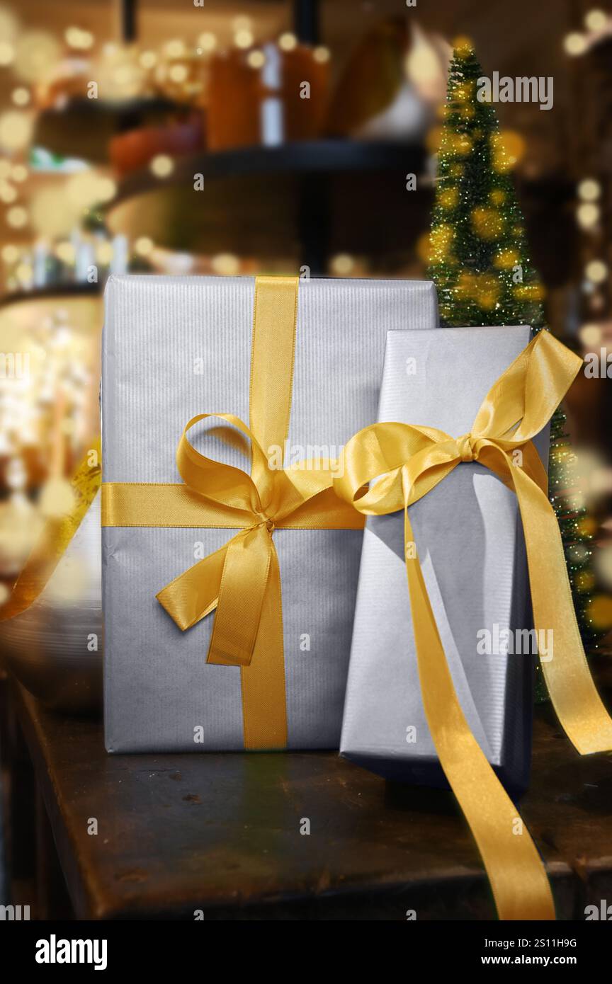 Nastro d'oro intorno a due scintillanti regali di Natale, sullo sfondo un'atmosfera festosa sotto l'albero di Natale con bokeh d'oro. Foto Stock