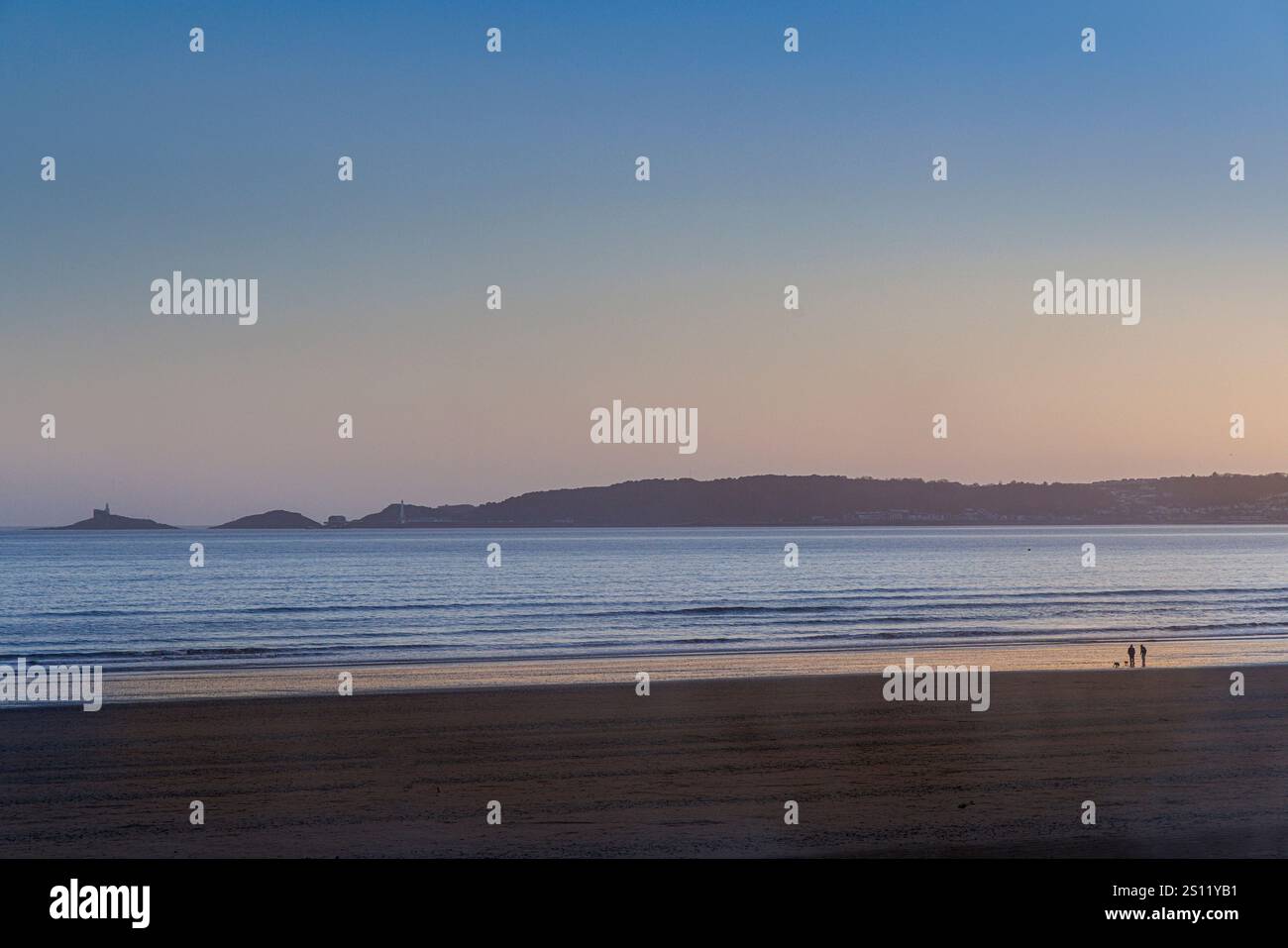 Persone sulla spiaggia di Swansea con il promontorio di Mumbles in lontananza, Gower, Galles, Regno Unito Foto Stock