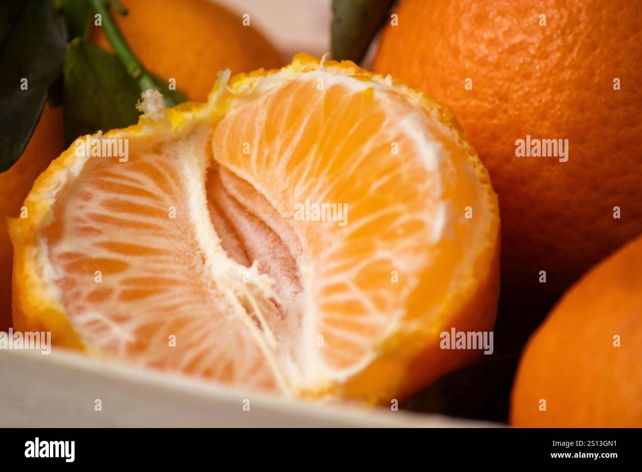 Primo piano di mandarini interi e un frutto pelato in una scatola di legno su sfondo grigio Foto Stock