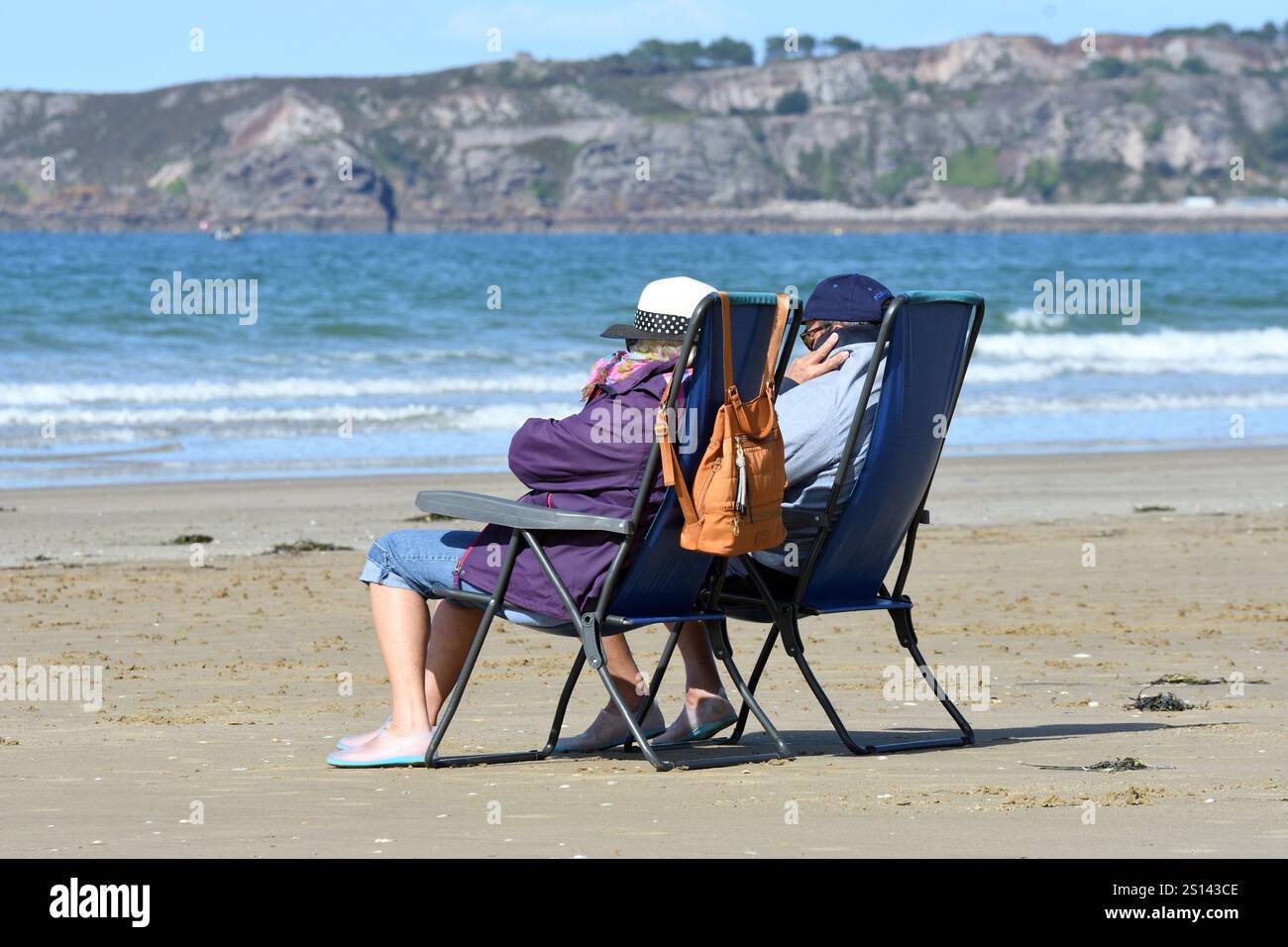 Coppia seduta su sedie da campeggio sulla spiaggia e sfidando il maltempo, Francia, Bretagna, Erquy Foto Stock