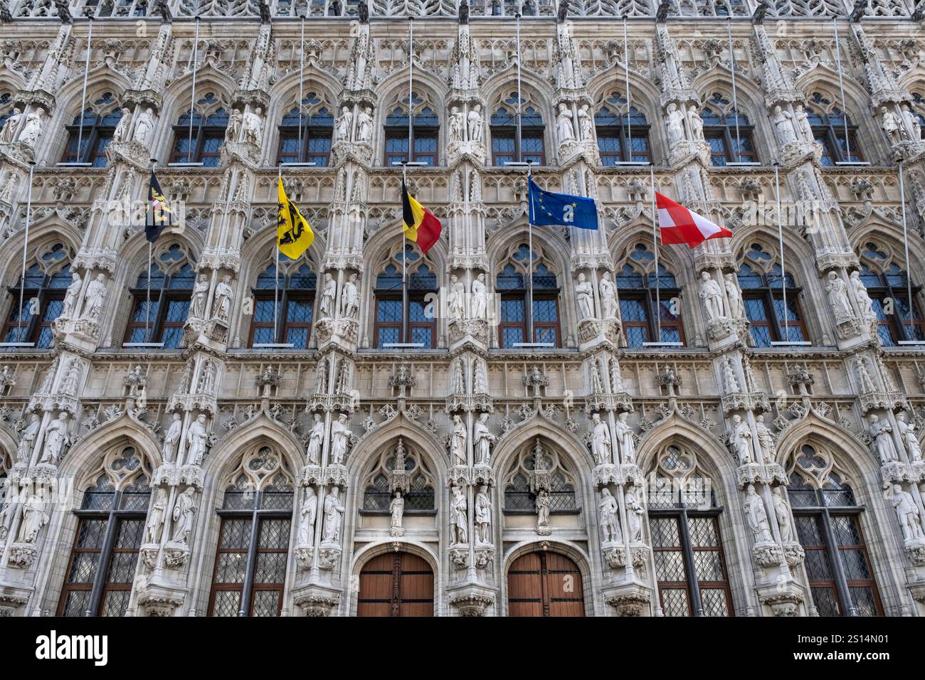 Facciata riccamente decorata del municipio di Lovanio, con consolle, sculture e bandiere del Belgio, dell'Europa e di alcune province del Belgio Foto Stock