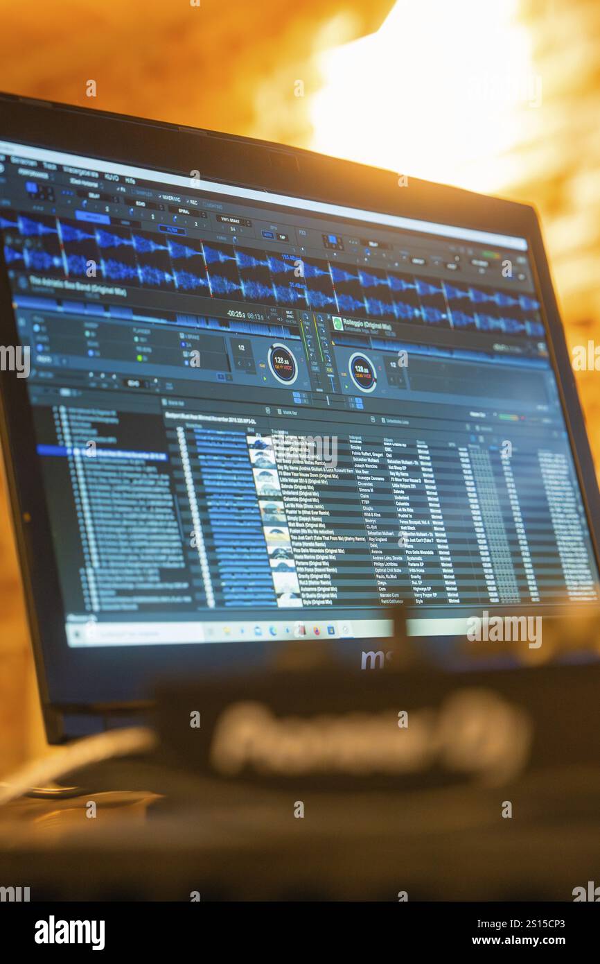 Un monitor mostra il software DJ con un'interfaccia utente blu e una luce calda sullo sfondo Foto Stock