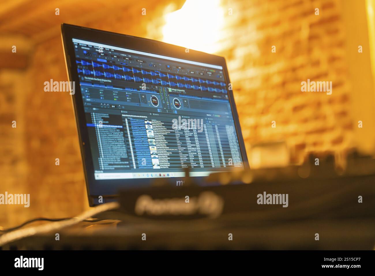 Schermo con software DJ e interfaccia utente blu, circondato da una calda luce di sfondo Foto Stock