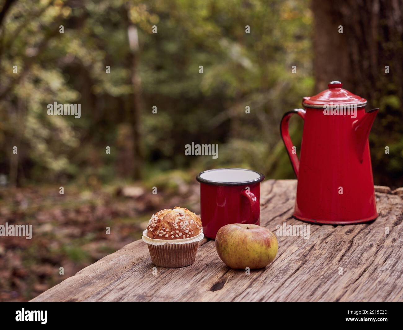 Picnic invernale nella foresta. Caffettiera rossa vintage e tazza, cupcake e mela su un tavolo di legno. Ambiente naturale e comfort, momento di calma Foto Stock