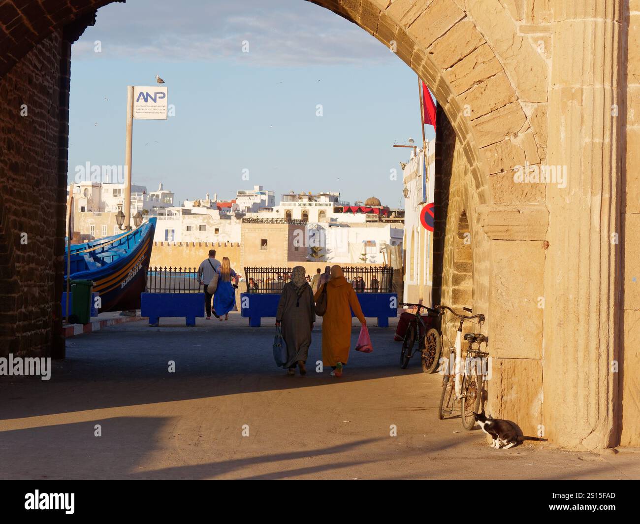 Una donna del posto cammina sotto un arco verso la storica Medina con la barca da pesca lasciata nella città di Essaouira, il 31 dicembre 2024 Foto Stock