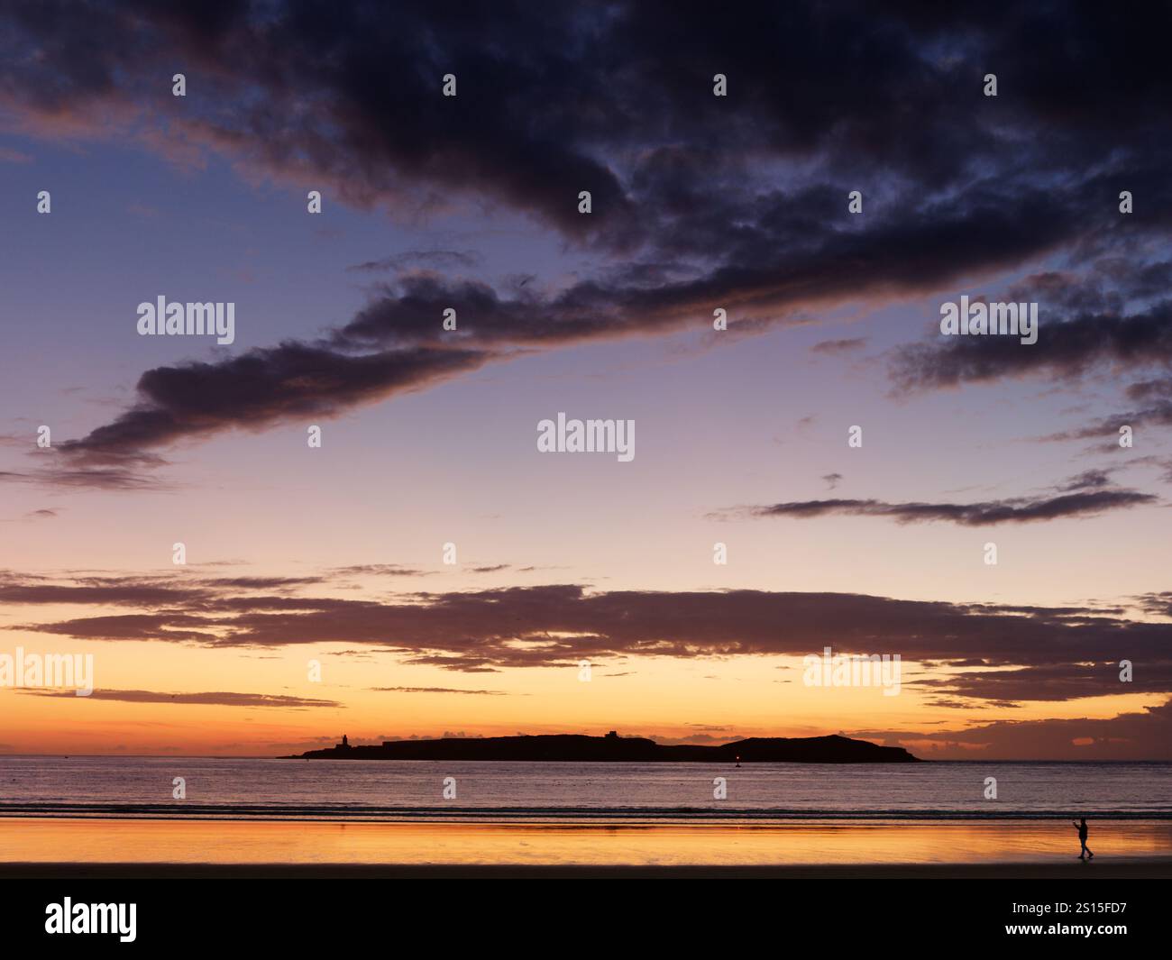 Cielo spettacolare al tramonto su un'isola sul mare Atlantico mentre qualcuno cammina sulla spiaggia in silhouette nella città di Essaouira, 31 dicembre 2024 Foto Stock