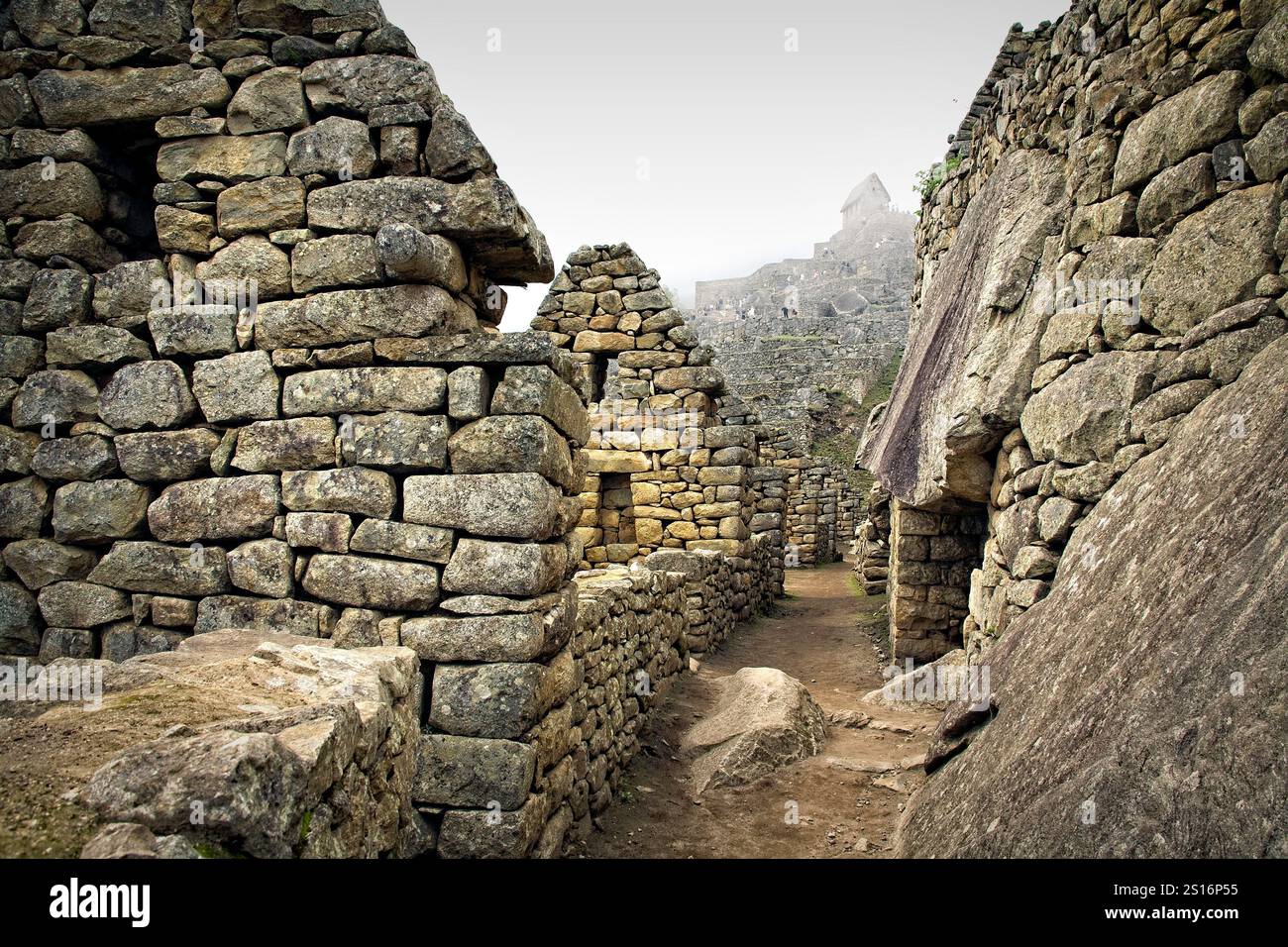 Le intricate pietre degli antichi edifici di Machu Picchu, con l'iconica casa di guardia che si erge maestosamente in lontananza. Foto Stock