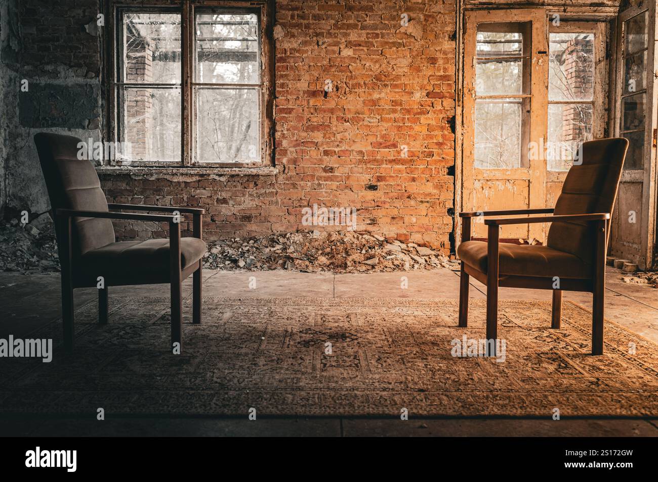 Due sedie vintage si affacciano in una stanza abbandonata con pareti in mattoni, finestre rotte e una porta intemprata, creando un'atmosfera nostalgica e urbana Foto Stock