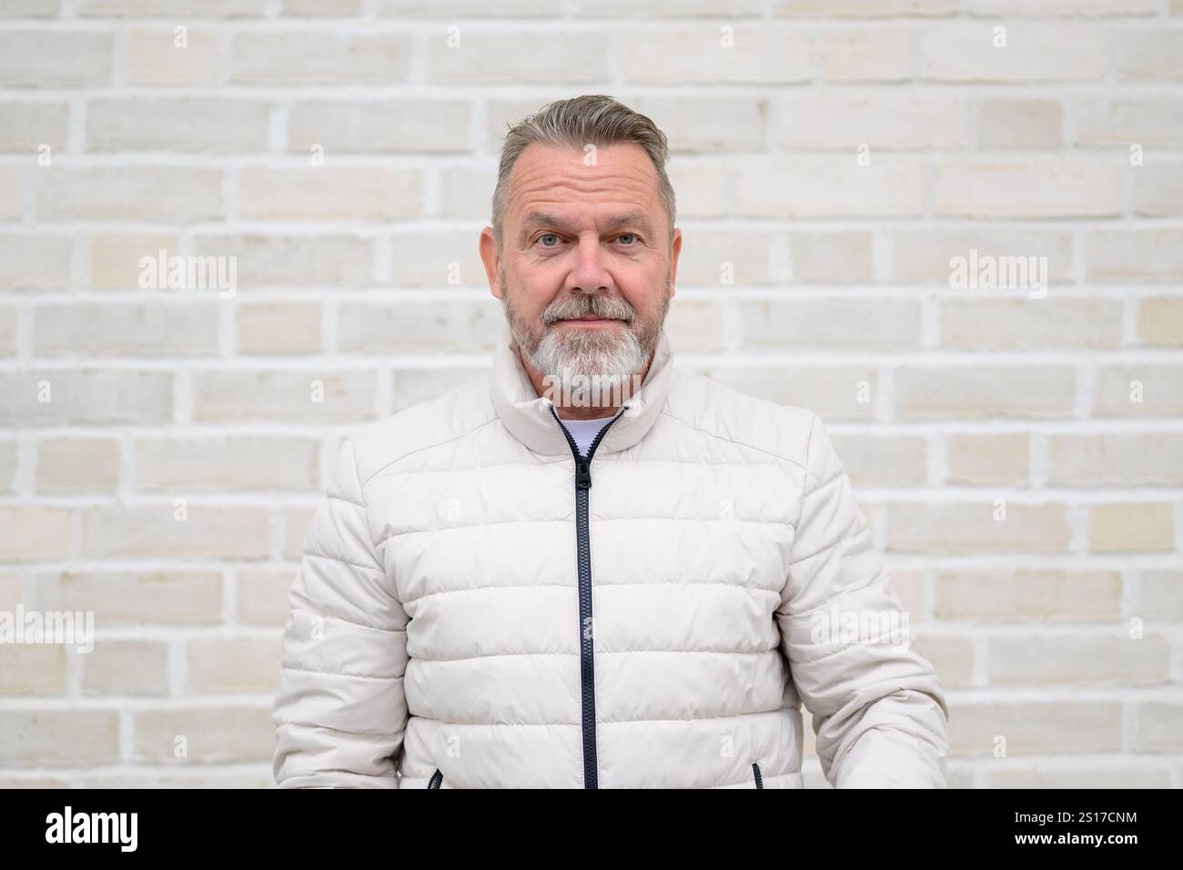 Ritratto di un uomo maturo con barba grigia, giacca trapuntata di colore chiaro e sguardo sicuro nella fotocamera. Foto Stock