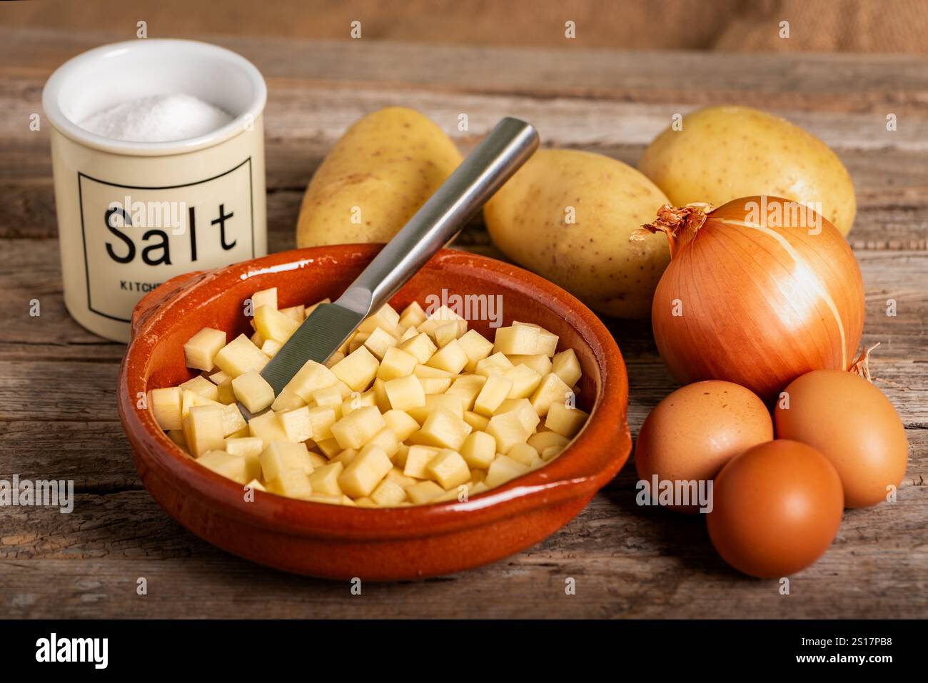 Ingredienti per cucinare una frittata di patate spagnola: Patate a dadini, cipolla, uova e sale, su un rustico tavolo di legno Foto Stock