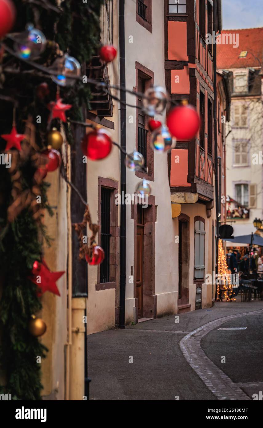 Le stelle rosse e gli splendidi ornamenti natalizi sono appesi a un ramo dell'albero di Natale lungo una strada acciottolata fiancheggiata da edifici in legno, Colmar, Francia Foto Stock