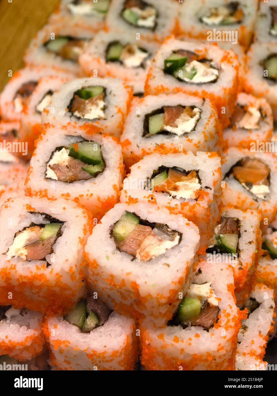 Pile di vivaci sushi roll presentano strati di pesce fresco, cetrioli croccanti e ripieno cremoso, il tutto avvolto in un tobiko arancione brillante. Un culi delizioso Foto Stock