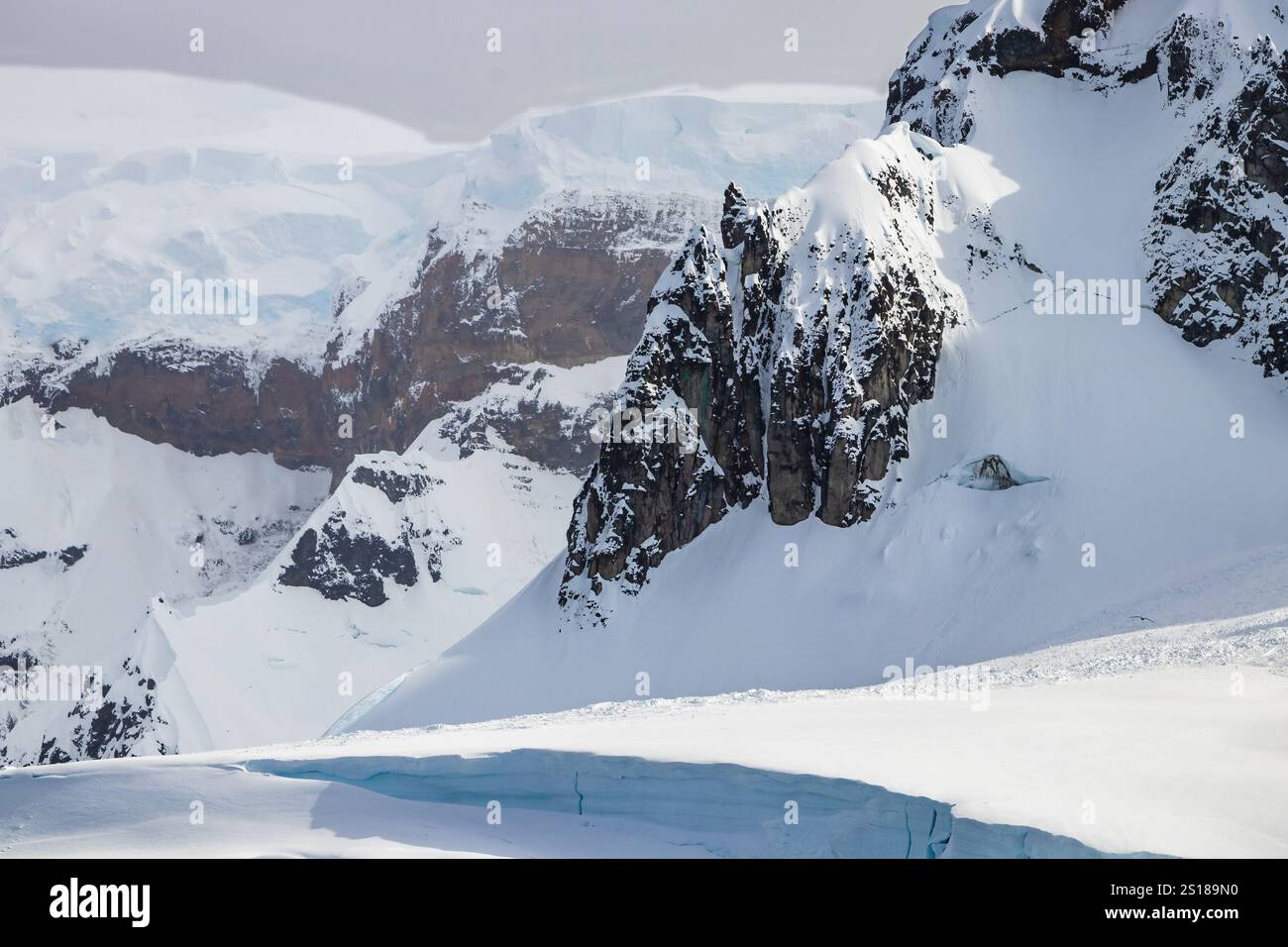 Terreno montano estremo sulla penisola antartica. Rocce taglienti che sporgono attraverso la neve profonda sui ripidi pendii. Foto Stock