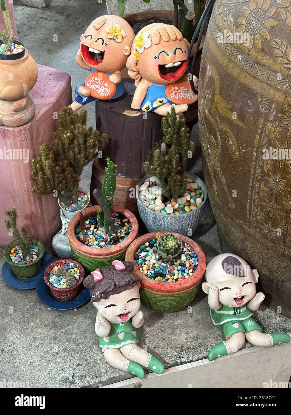 Varie statuette in ceramica impilate con cura dalle vicine piante in vaso Foto Stock