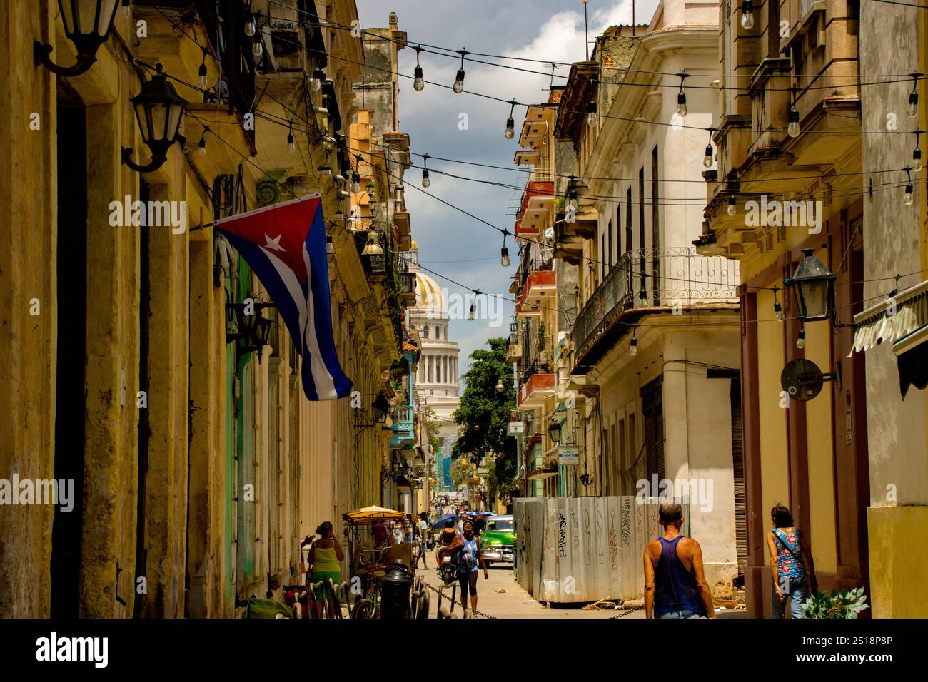 Fotografia di una strada a l'Avana che conduce al Capiitolio, che mostra una bandiera cubana, l'architettura coloniale e la vivace cultura. Foto Stock