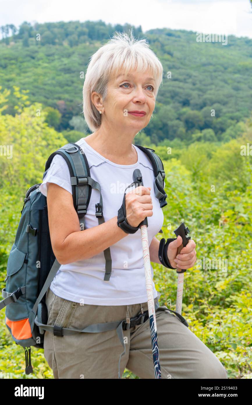 Una donna di 60-65 anni sta camminando attraverso la foresta con i bastoncini da nordic walking. Foto Stock
