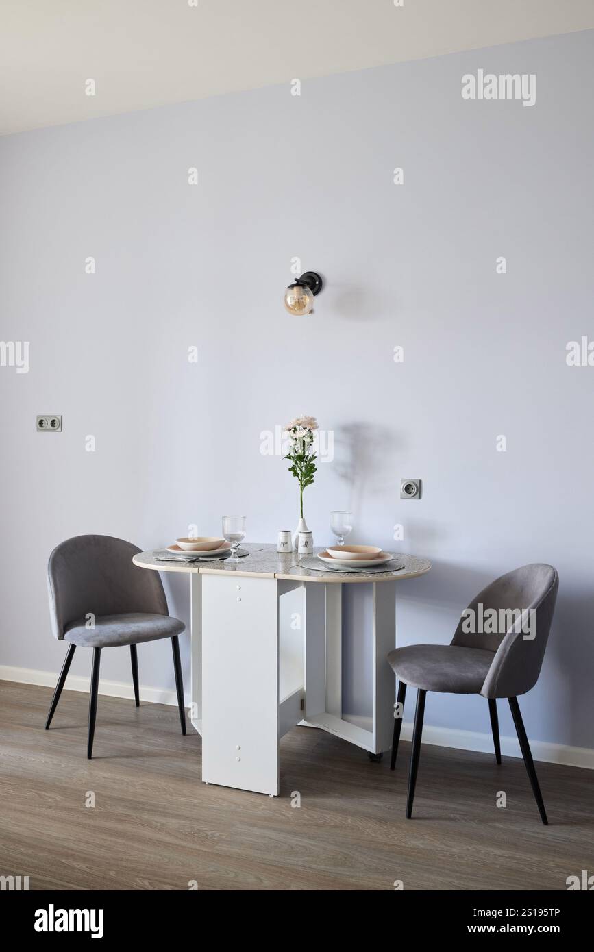 Un'elegante ed elegante sala da pranzo con tavolo rotondo, abbinata a due eleganti sedie su un morbido sfondo viola Foto Stock