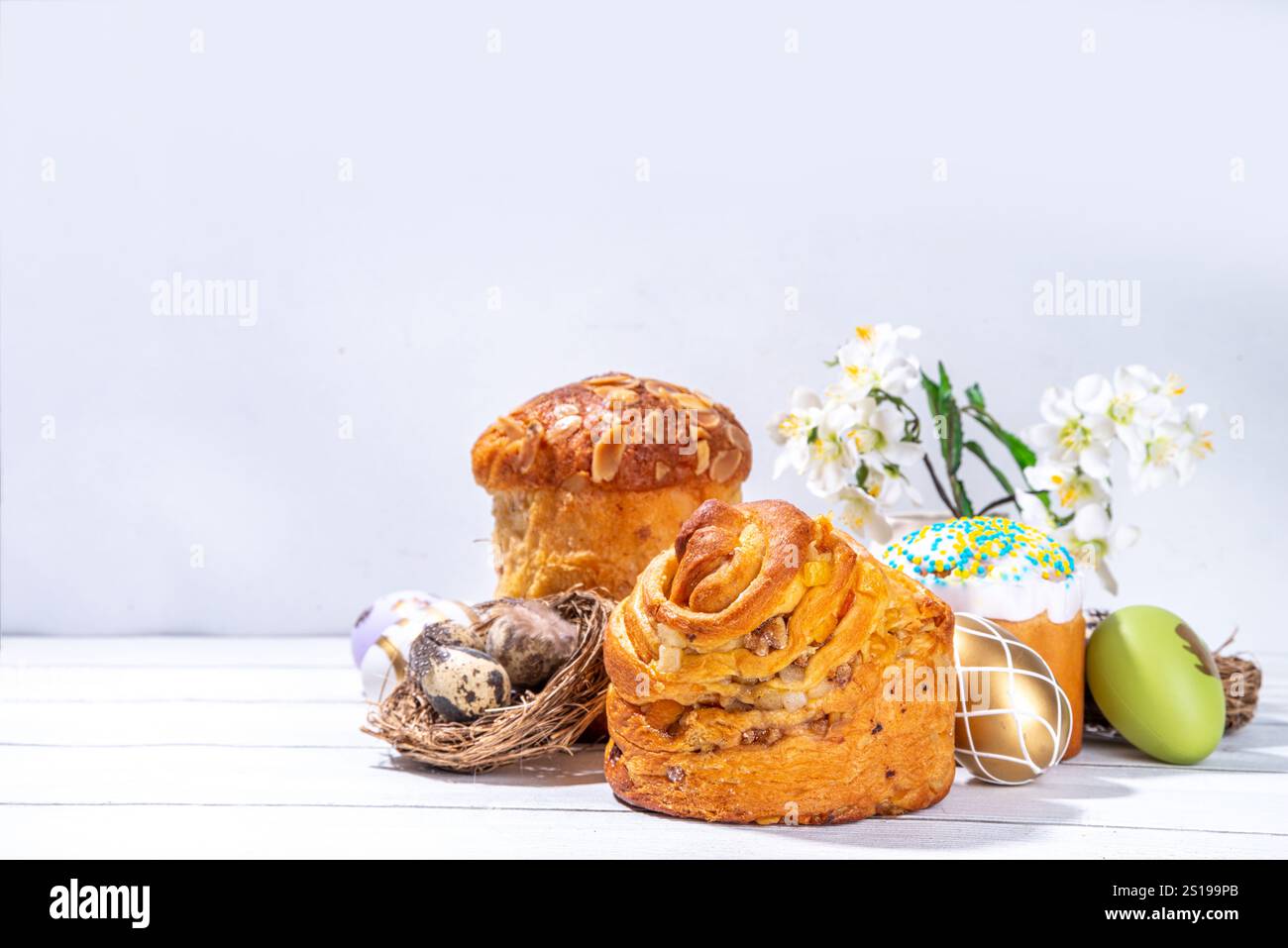 Sfondo pasquale con dolci tradizionali natalizi: Kraffin, panettone, paska kulich, uova pasquali, fiori primaverili su tavola bianca di legno, spiaggie Foto Stock