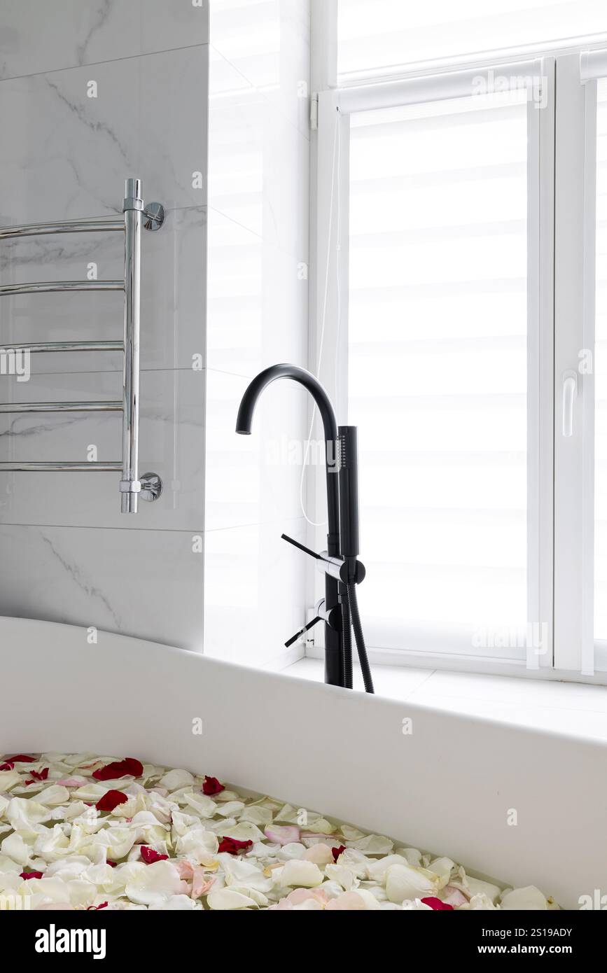 Vasca da bagno contemporanea con un elegante rubinetto nero circondato da morbidi petali di rosa Foto Stock