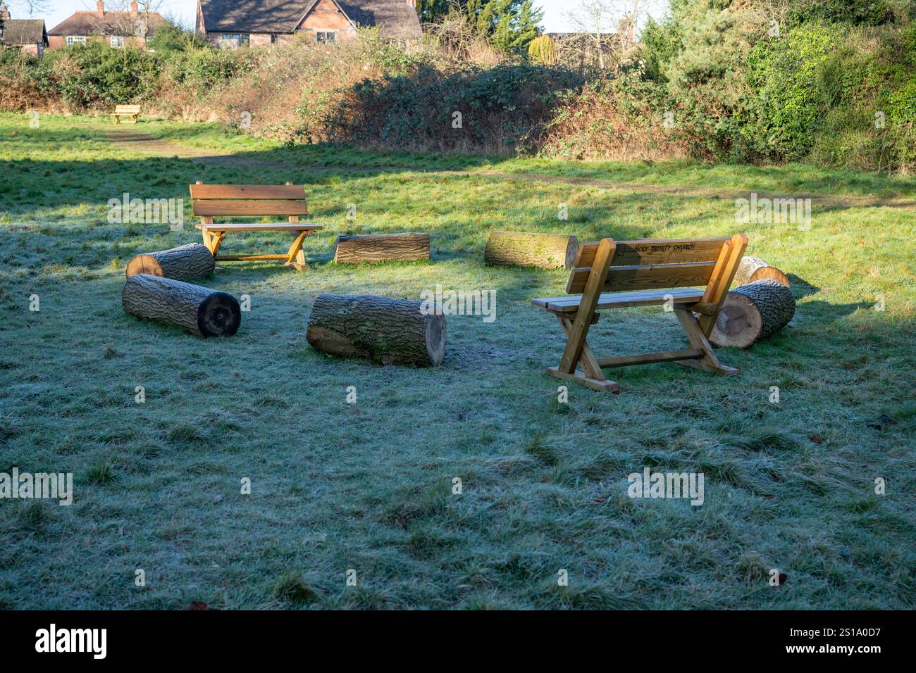 Una cerchia di posti a sedere, tra cui panche e tronchi di legno, nell'angolo di un piccolo campo accanto a una chiesa vista in una fredda giornata di sole d'inverno. Foto Stock