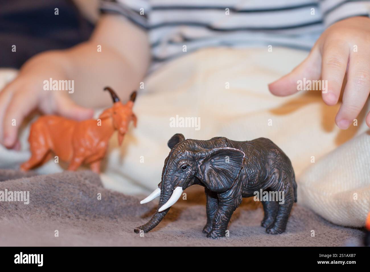 Un bambino gioca con un piccolo elefante giocattolo nero e un cervo giocattolo rosso Foto Stock