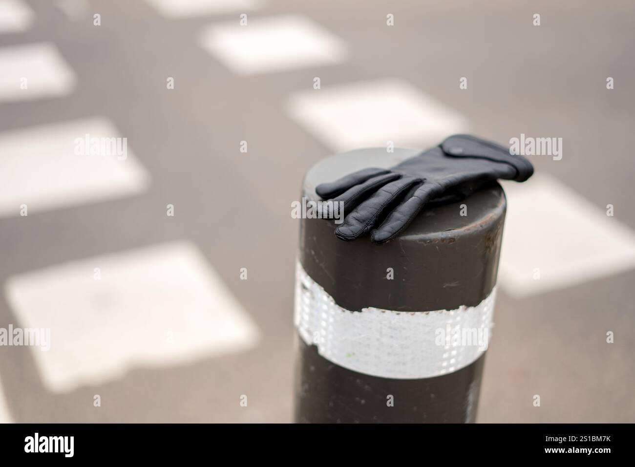 Guanto in pelle Photo Black appoggiato sul paletto metallizzato nell'ambiente Urban Crosswalk crea Sense of Mystery e Intrigue nell'incontro quotidiano con il paesaggio urbano Foto Stock
