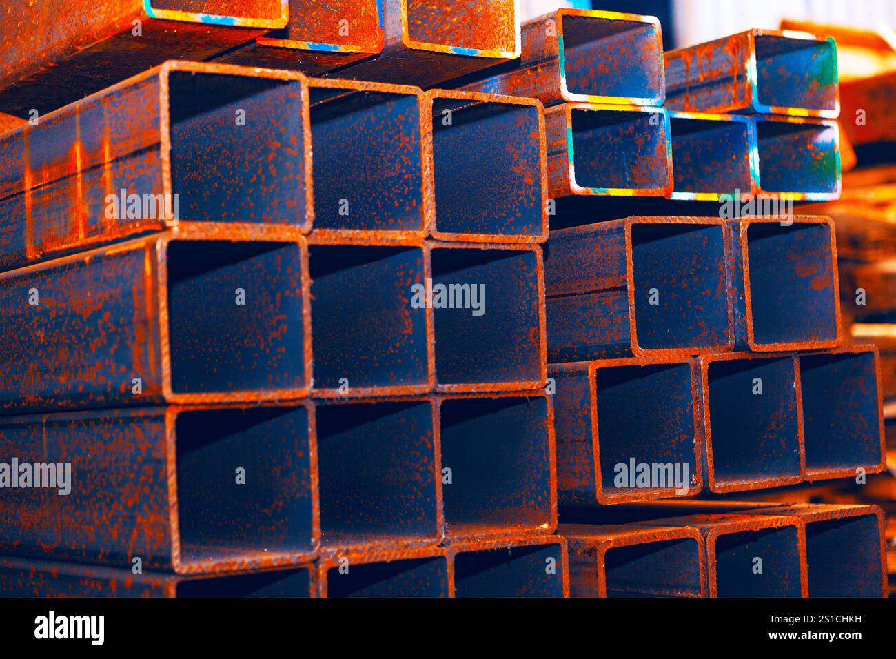Pila di tubi di acciaio cavi rettangolari con superficie arrugginita. La scena industriale evidenzia gli effetti dell'ossidazione sul metallo e suggerisce possibili utilizzi per Foto Stock