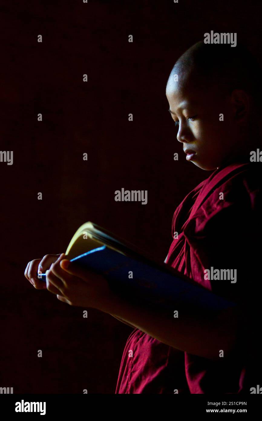 Ritratto a luce bassa della lettura di un giovane monaco novizio all'interno dell'antico tempio di Bagan, Old Bagan, Nyaung U, Myanmar Foto Stock