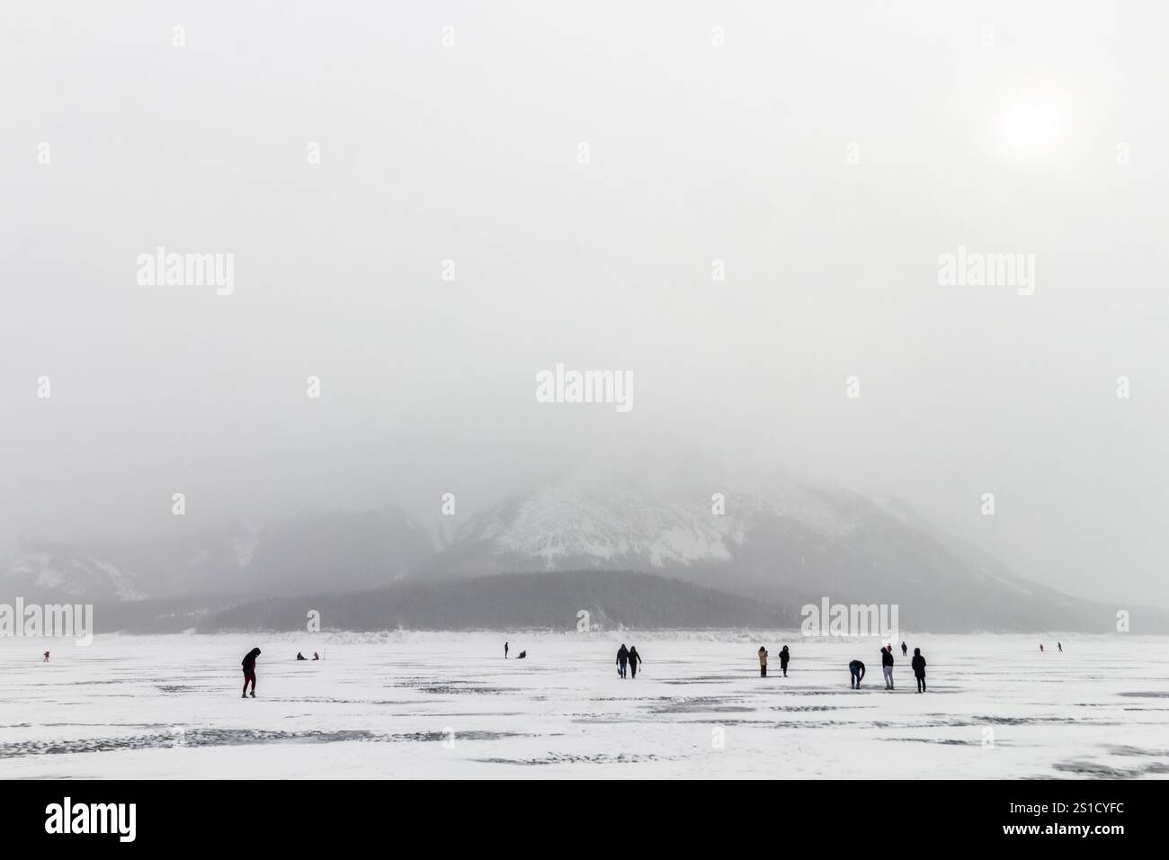 Vista panoramica del lago Abraham ghiacciato nebbioso in Alberta, Canada, con i visitatori che camminano sulla superficie ghiacciata, annacquata dal vasto paesaggio invernale Foto Stock