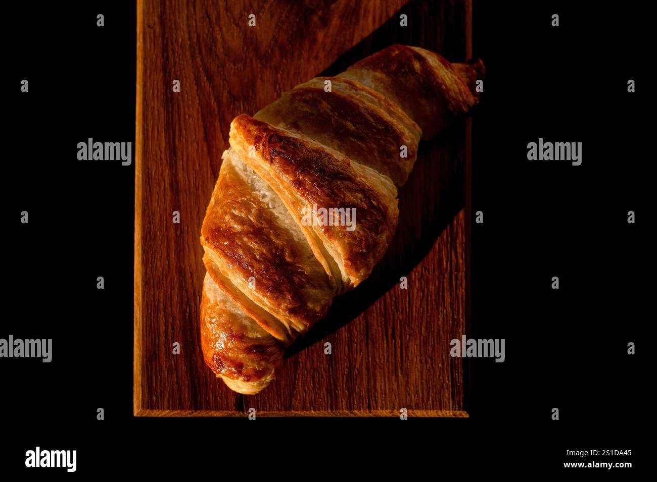 Croissant croccante marrone su un vassoio di legno Croissant francese a base di farina e burro. Croissant appena sfornato su sfondo nero. Foto Stock