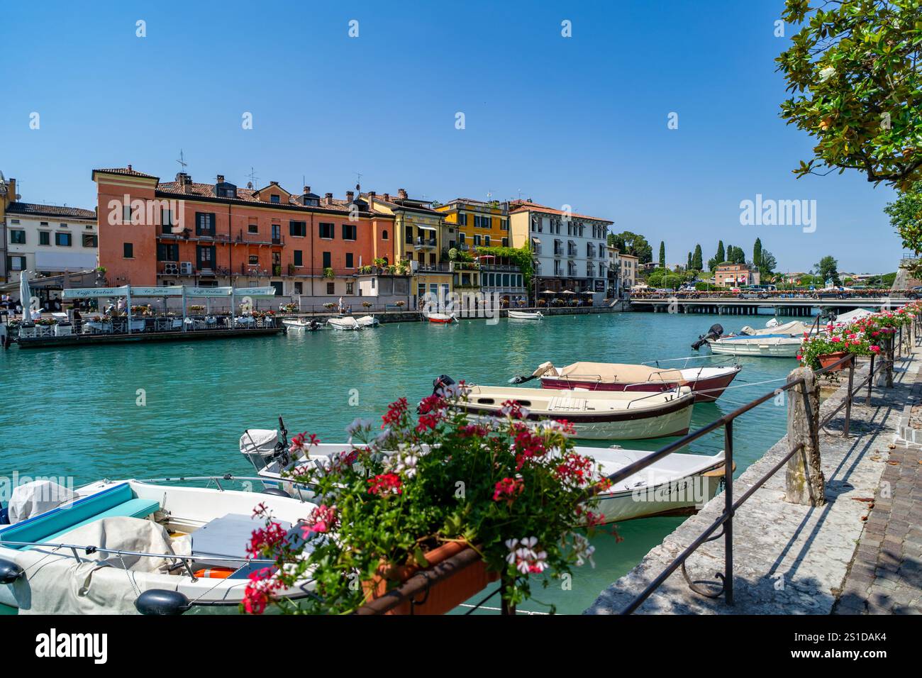 Incantevole vista sul canale con piccole barche ormeggiate lungo il lungomare, vivaci composizioni floreali in primo piano e colorati edifici italiani che fiancheggiano Foto Stock
