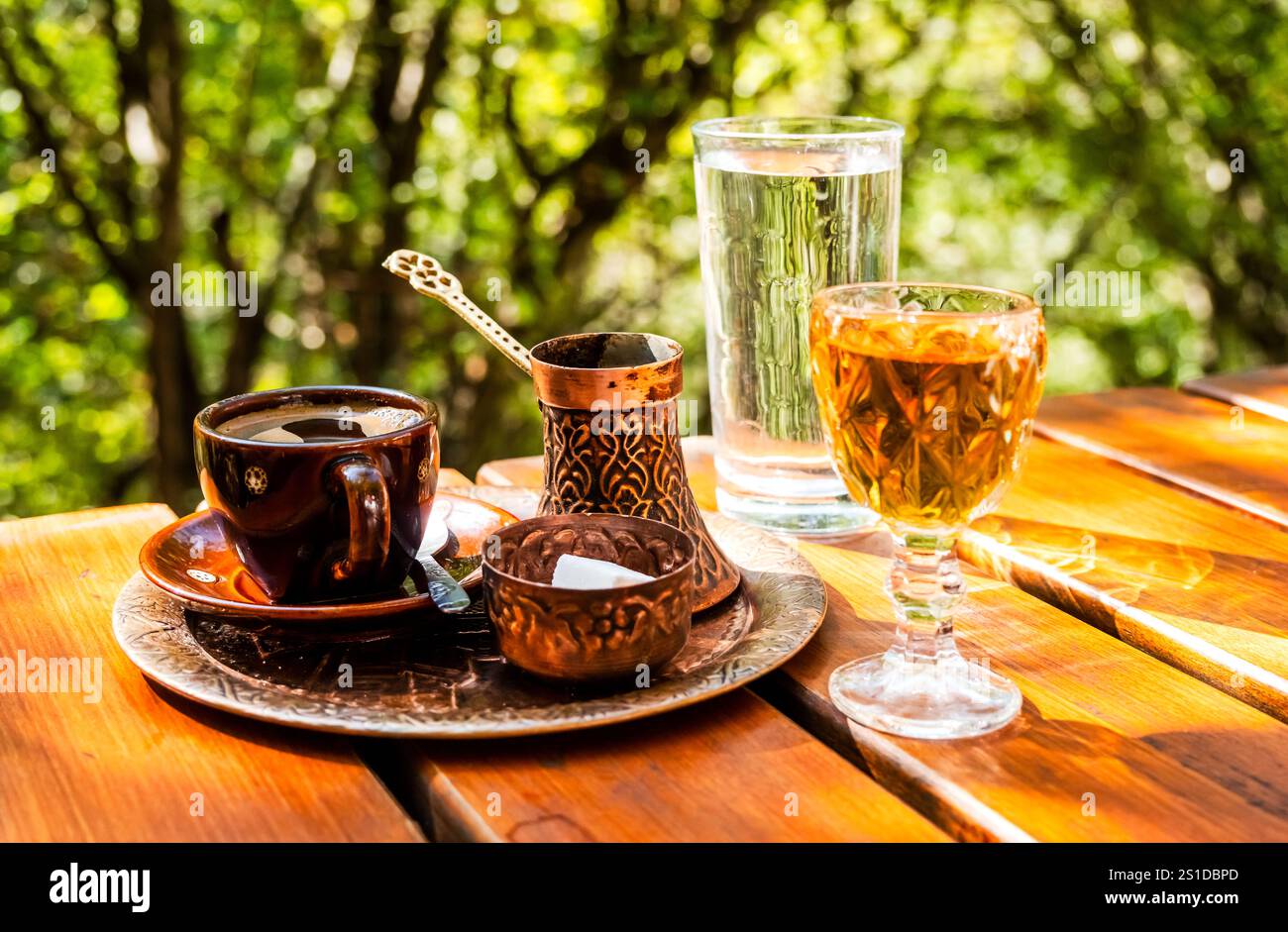 Caffè nero in una tazza, caffettiera vintage in rame e un bicchiere di brandy domestico su un rustico tavolo in legno Foto Stock