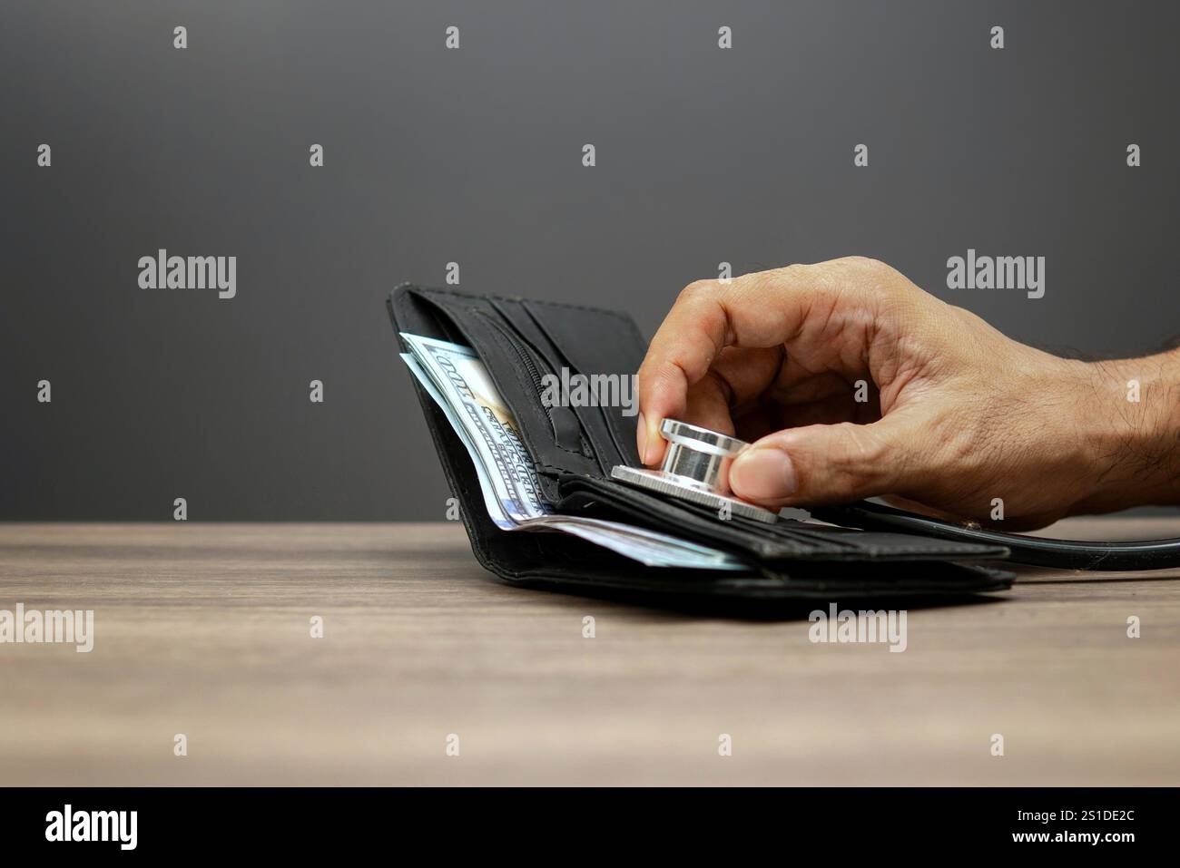 Una mano tiene uno stetoscopio su un portafoglio aperto con soldi all'interno, simboleggiando il concetto di salute e stato finanziario. Foto Stock