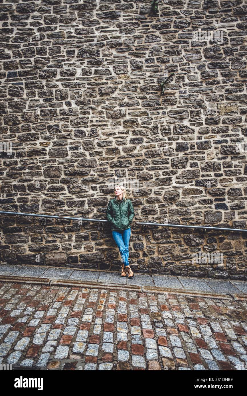 Bella giovane donna bionda si appoggia contro il muro di pietra in Quebec Foto Stock