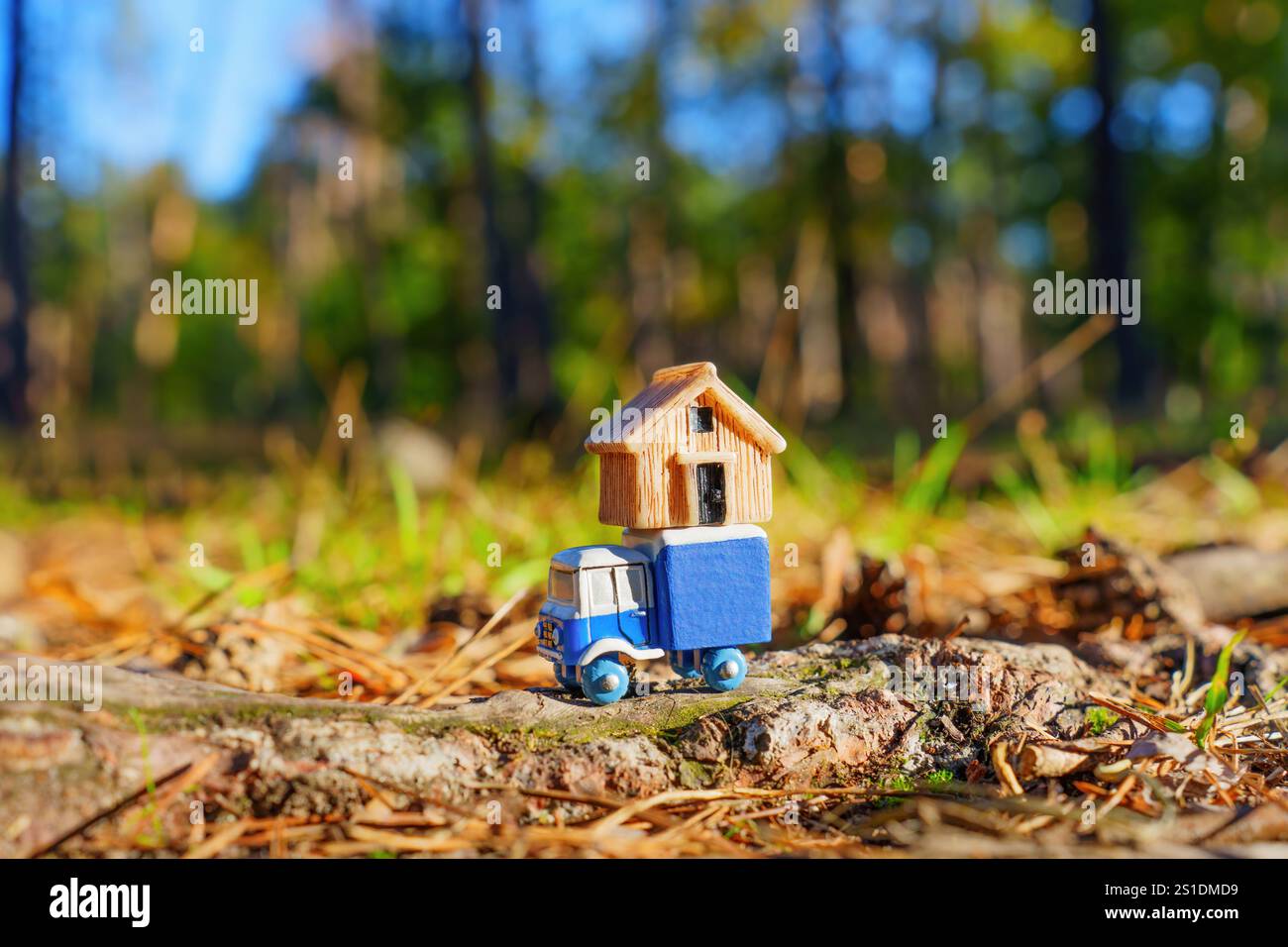 Camion in miniatura che trasporta una casa di legno su un tronco, circondato dalla natura, che illustra il fascino di vivere vicino alla natura o nelle aree rurali. Foto Stock